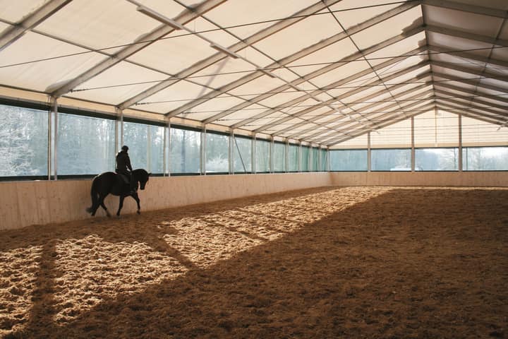 Indoor riding arena with a groomed fibre-and-sand surface, fresh harrow lines running down the long side