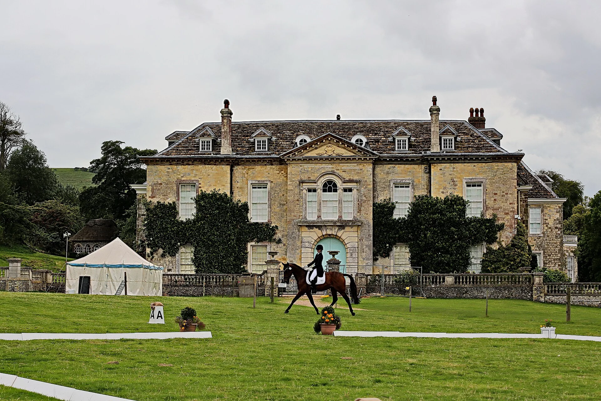 Rider competing in a grass dressage arena at Firle Place with the A marker and manor house beyond