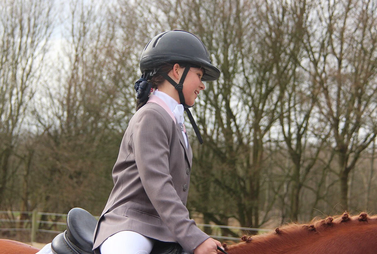 Young dressage rider standing beside her horse at a local competition