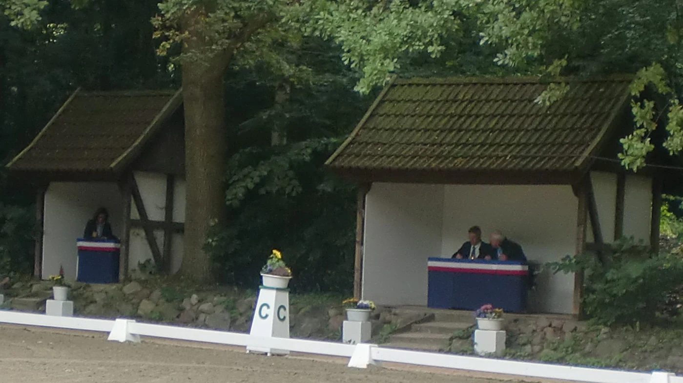 Dressage judging team seated beside an outdoor competition arena at Bad Segeberg
