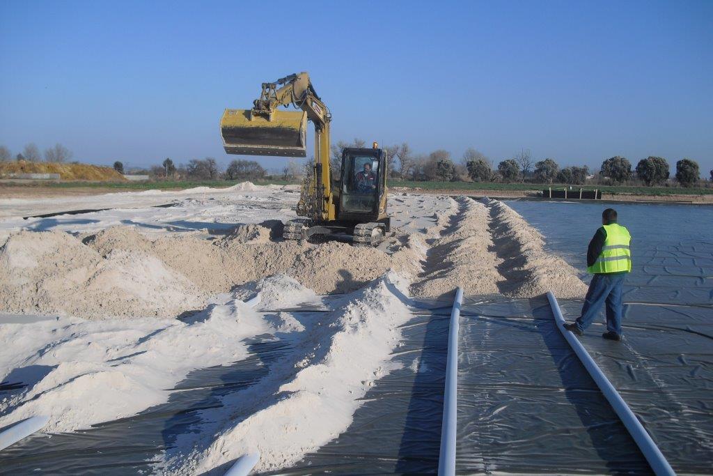 Riding arena under construction, with drainage lines and base layers of an ebb-and-flow subsurface watering system installed before the footing goes down