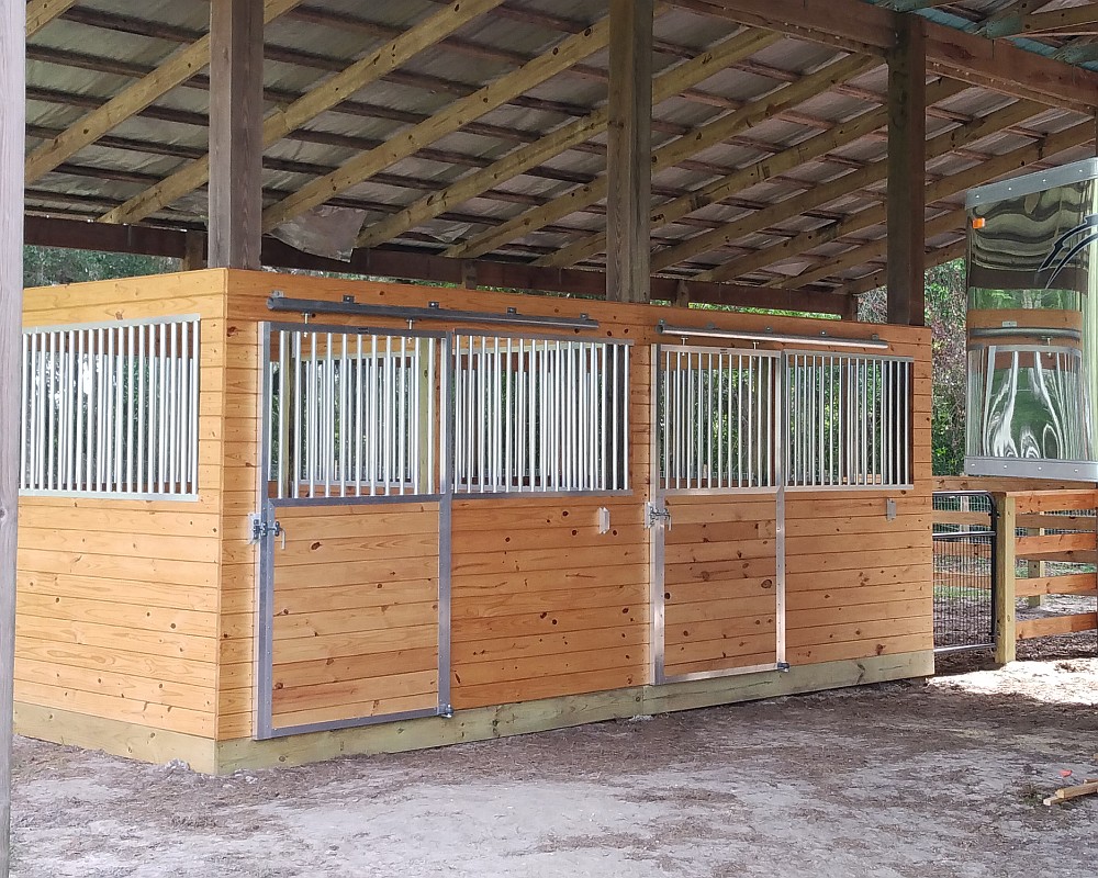 Wood-and-aluminum Armour stall fronts with sliding grille doors built into a covered open-air horse barn