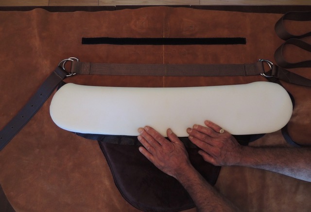 Hands fitting the removable foam insert into the El Compañero Bareback Rider pad, showing the stainless steel D-rings and girth strap