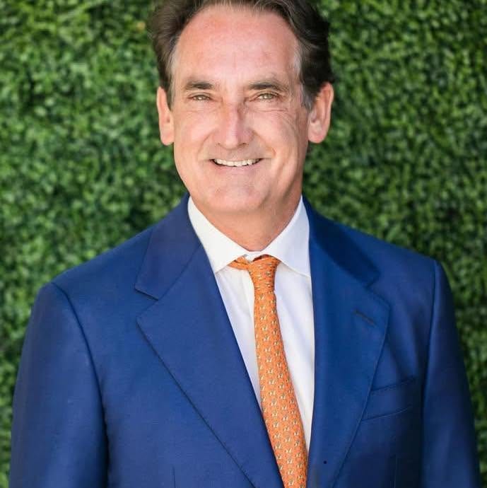 Equine attorney Bing I. Bush, Jr. in a navy blazer and orange tie in front of a green hedge wall