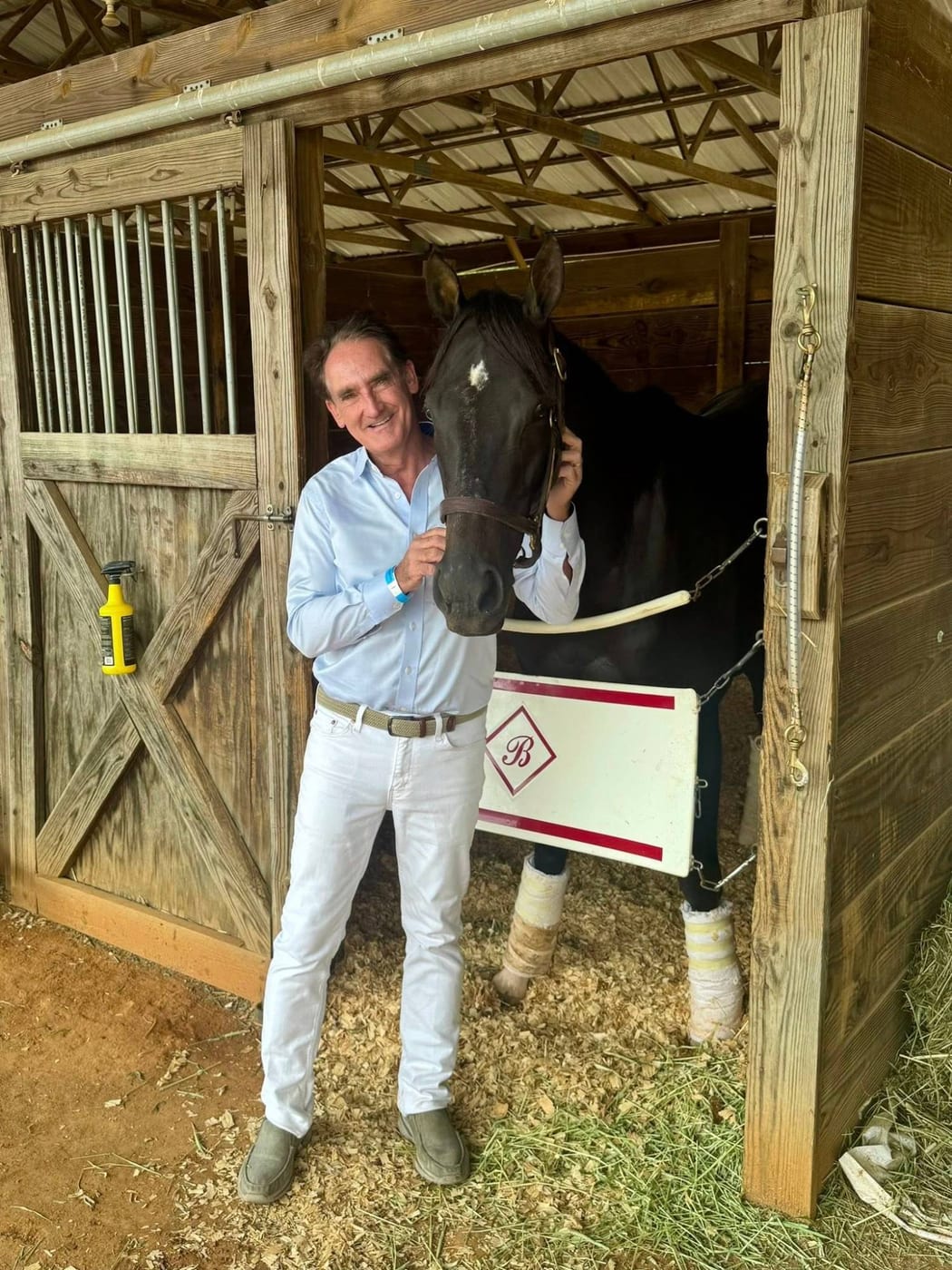 Bing Bush with a dark bay horse in standing wraps at an open stall door
