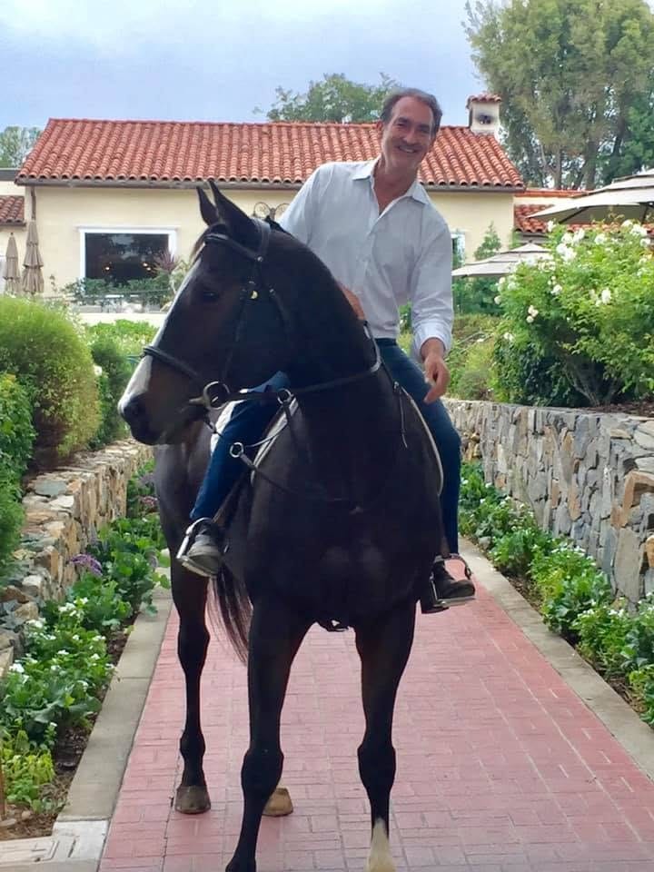 Bing Bush riding a dark bay horse along a brick garden path