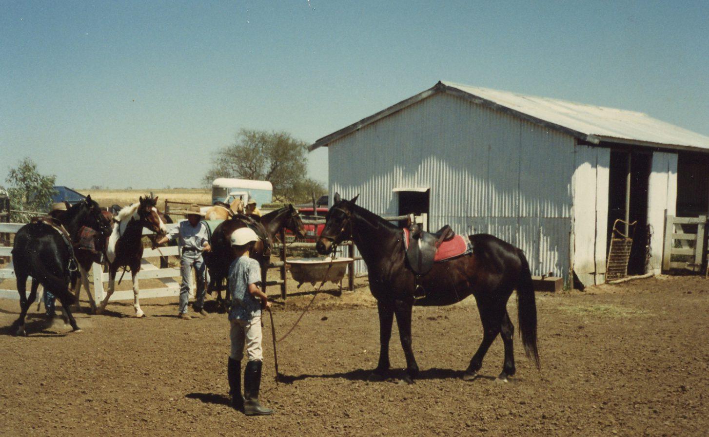 A young Clinton Anderson leading a saddled horse at an Australian training yard during the early apprenticeship years that shaped the Downunder Horsemanship Method