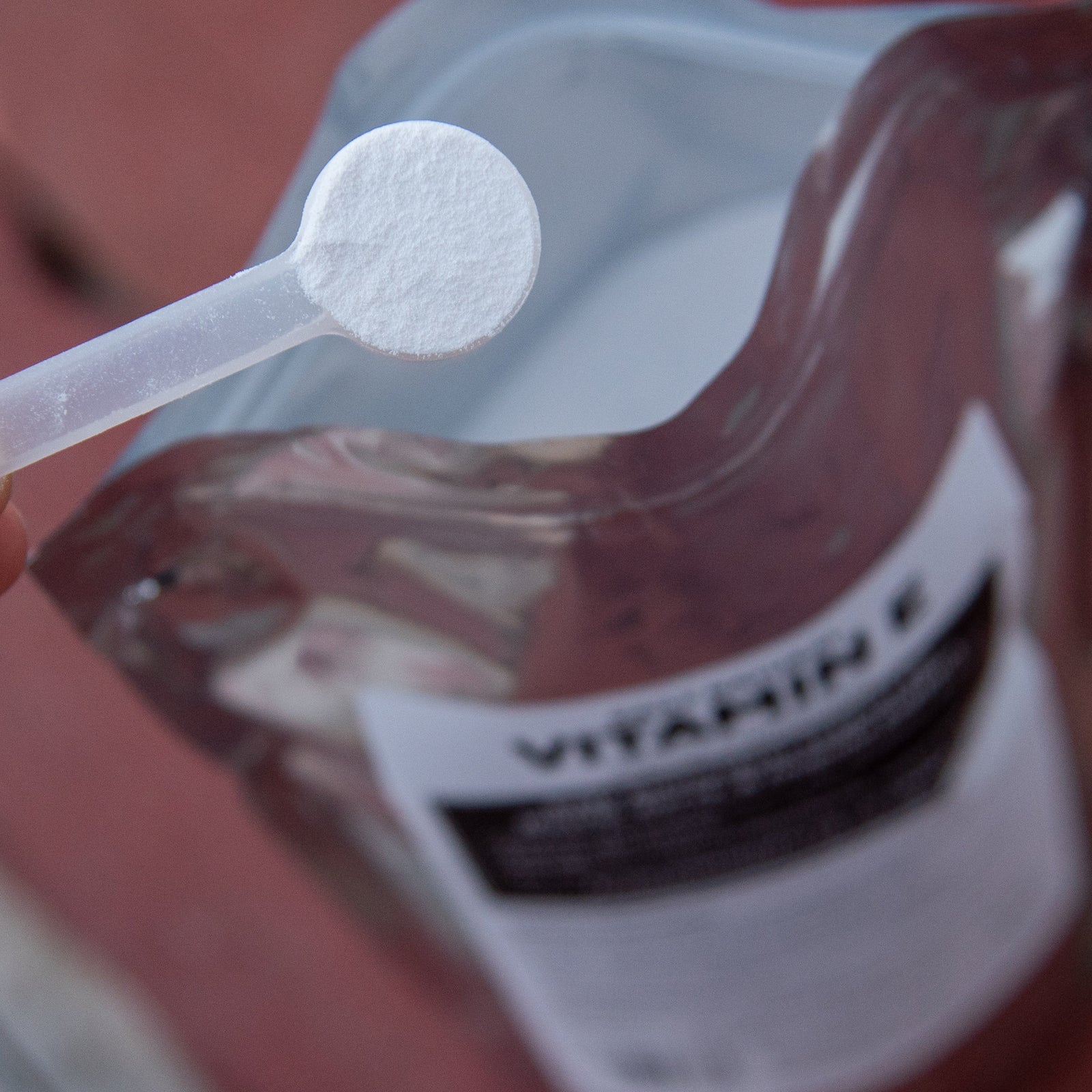 A measuring scoop of Daily, Natural Vitamin E powder held over the resealable supplement pouch