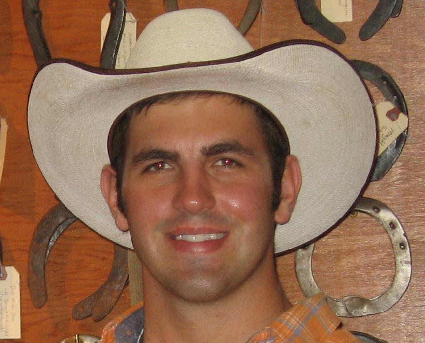 A working farrier graduate of the Butler program standing in front of a display wall of handcrafted horseshoes