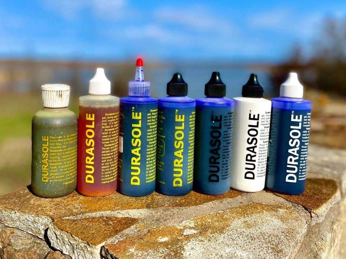 Lineup of Durasole bottles in several label colors and tip styles arranged on a stone wall outdoors