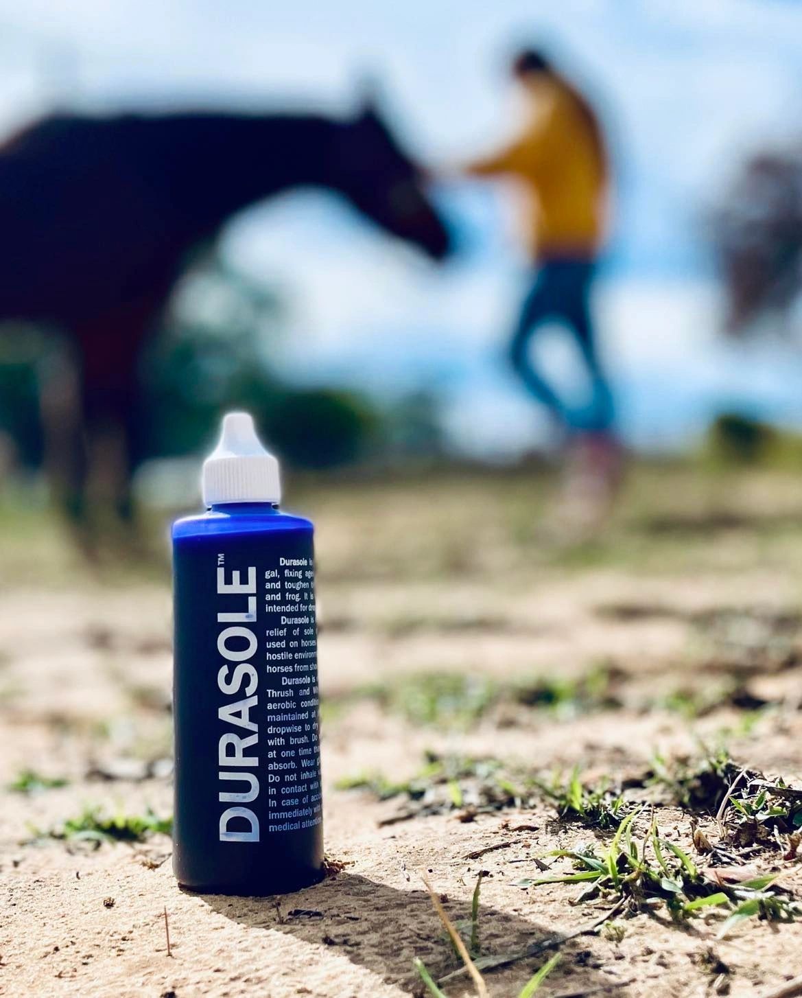 Durasole bottle standing in a dirt paddock with a horse and handler working in the soft-focus background