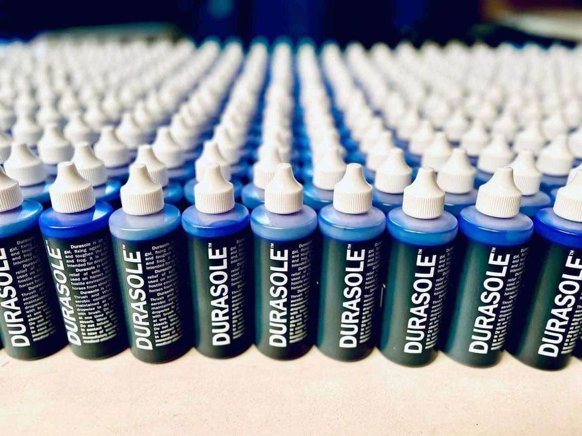 Hundreds of filled Durasole bottles lined up across a workbench during a production run