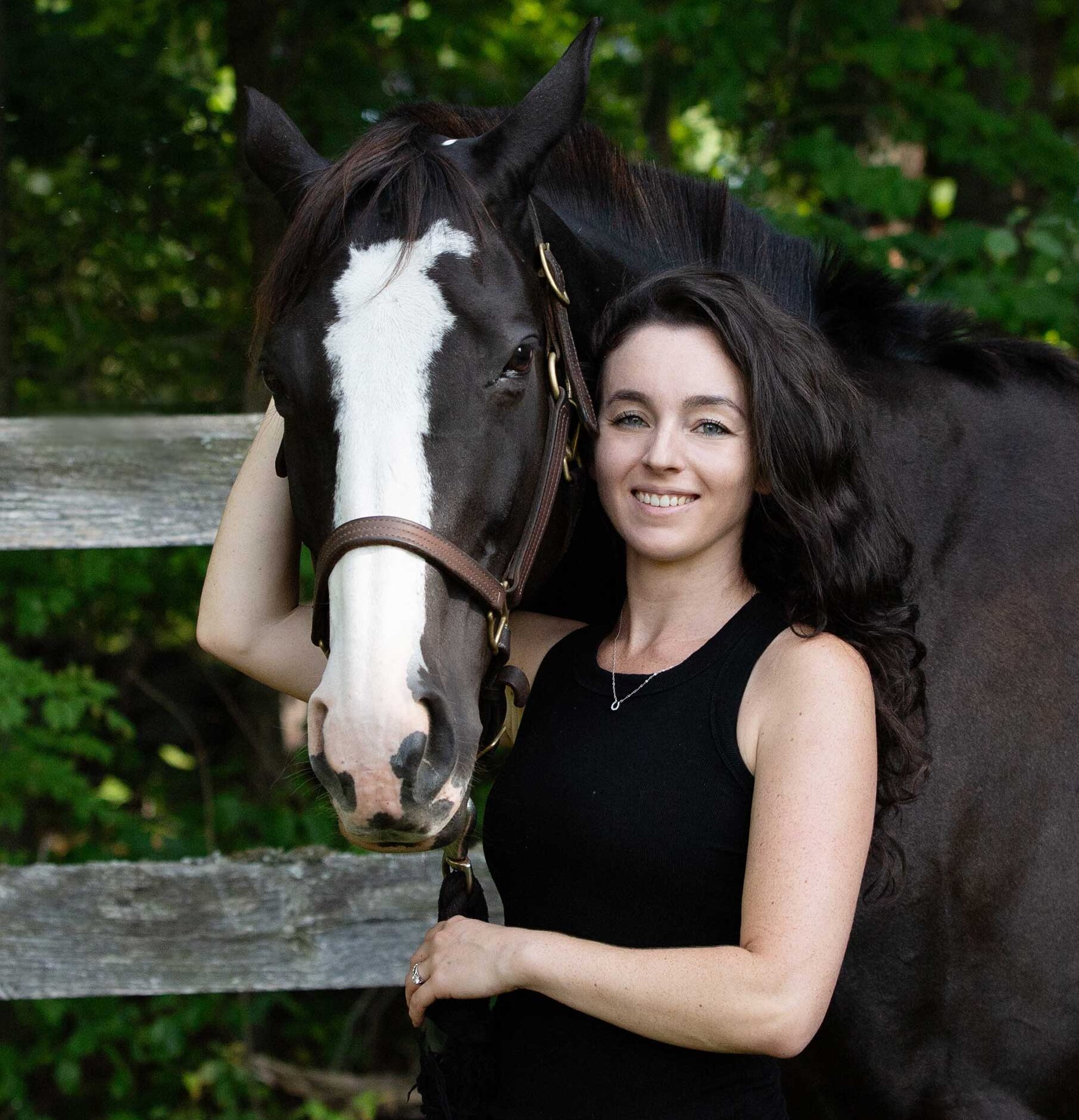 Jessica Dion smiling cheek to cheek with her dark horse beside a wooden fence