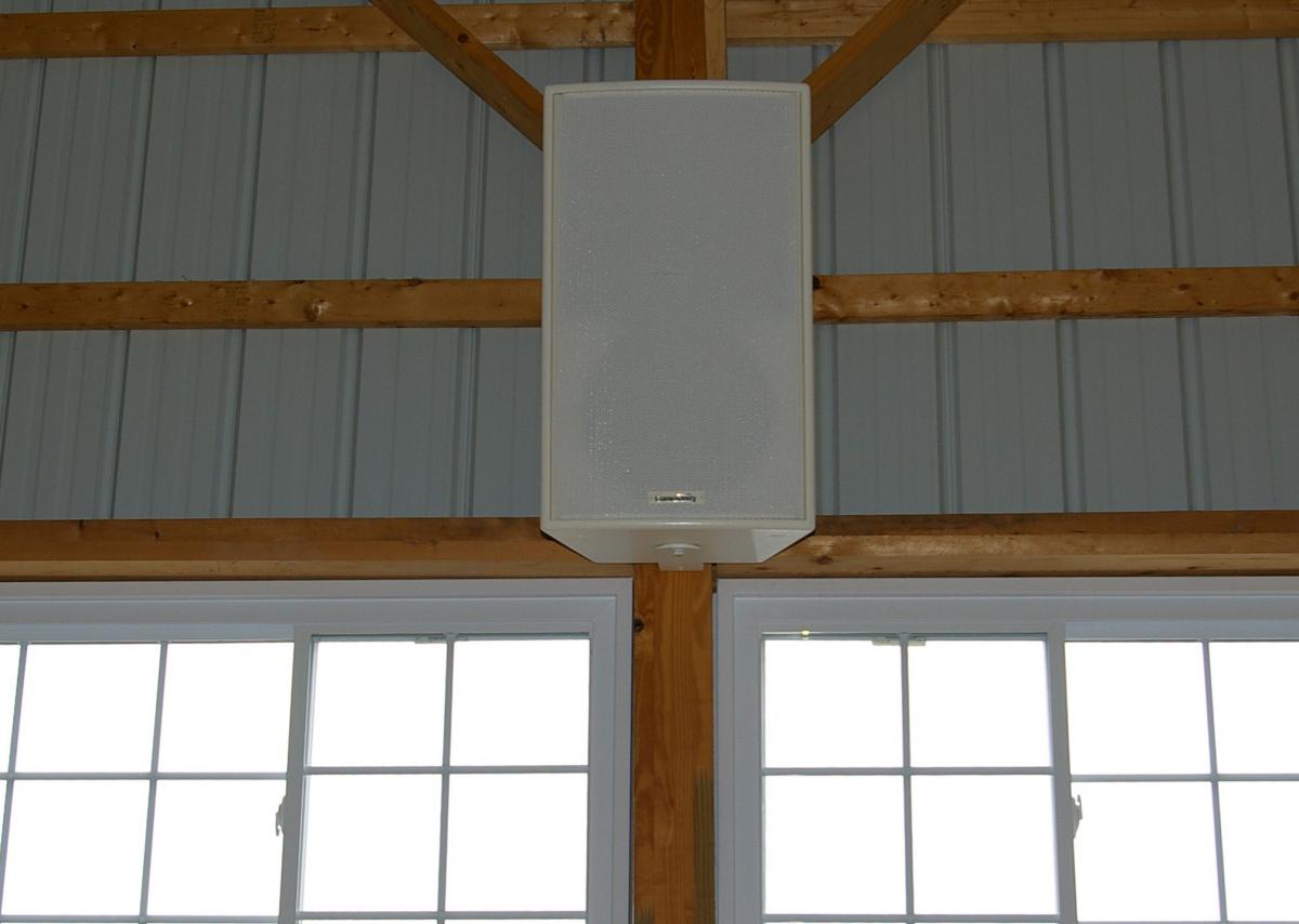 Weather-resistant white speaker mounted in barn rafters for background music in a horse stable