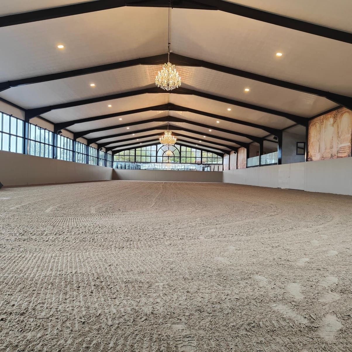 Freshly groomed indoor arena footing with even moisture throughout, under chandelier lighting