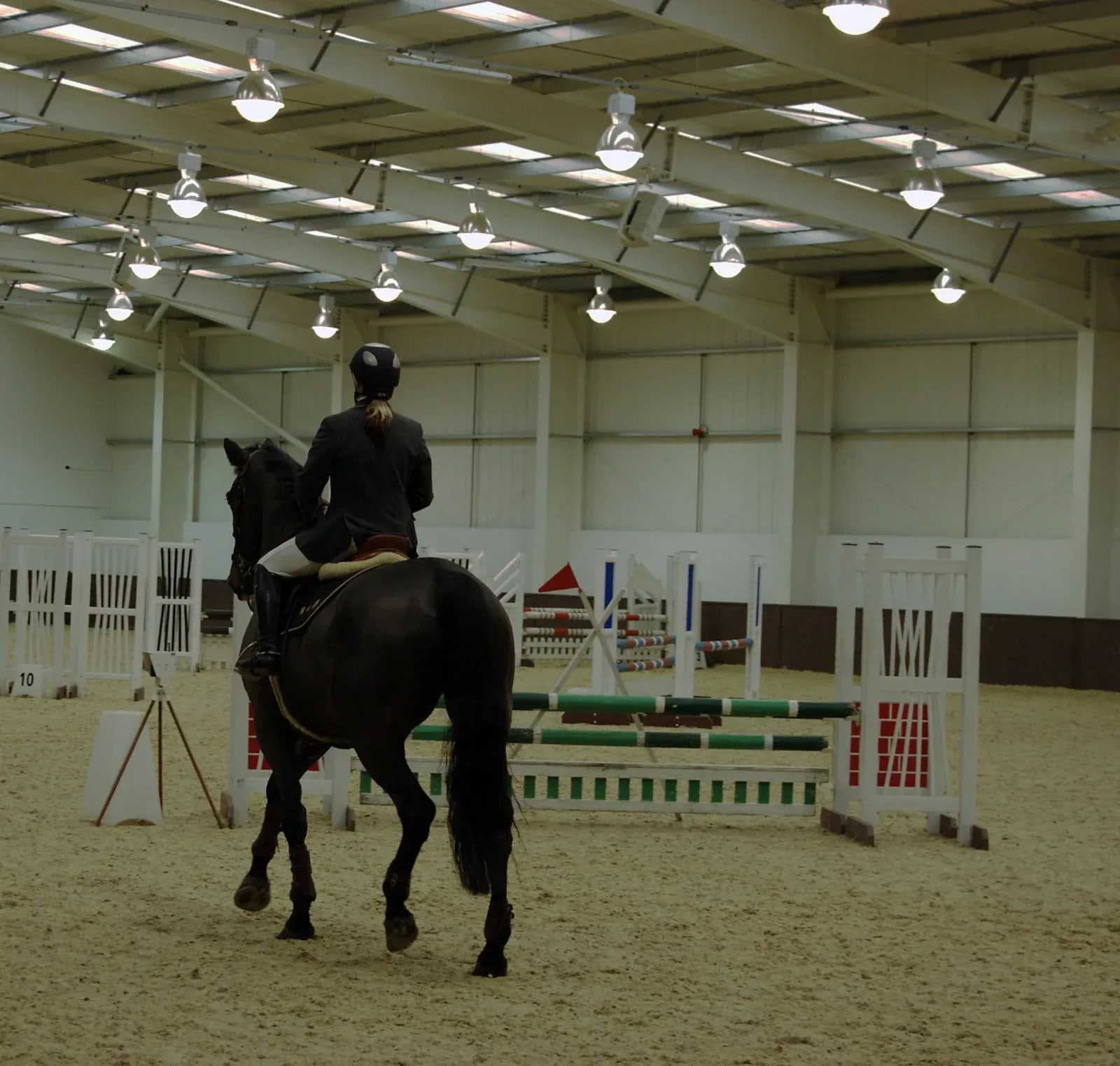 Indoor jumping arena with evenly watered sand footing, red steel roof trusses and skylights