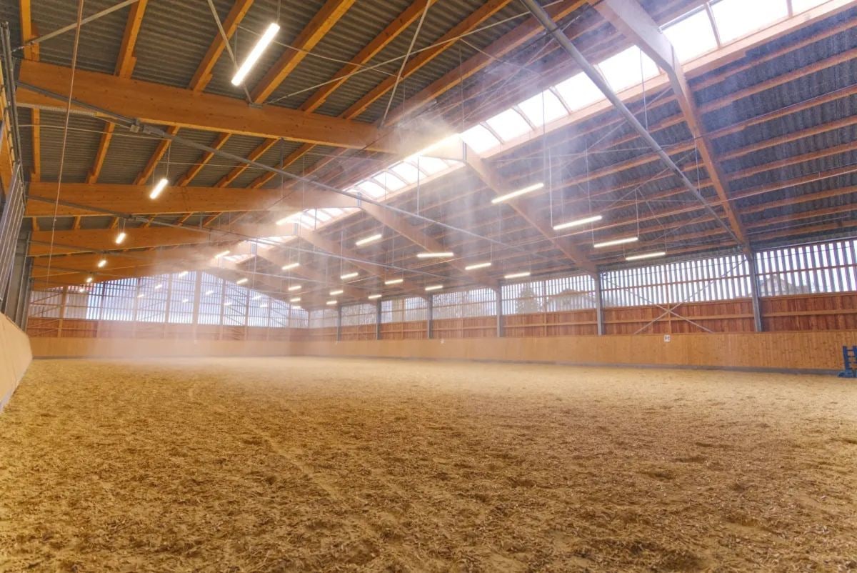 Overhead irrigation lines running the length of a timber-framed indoor riding arena