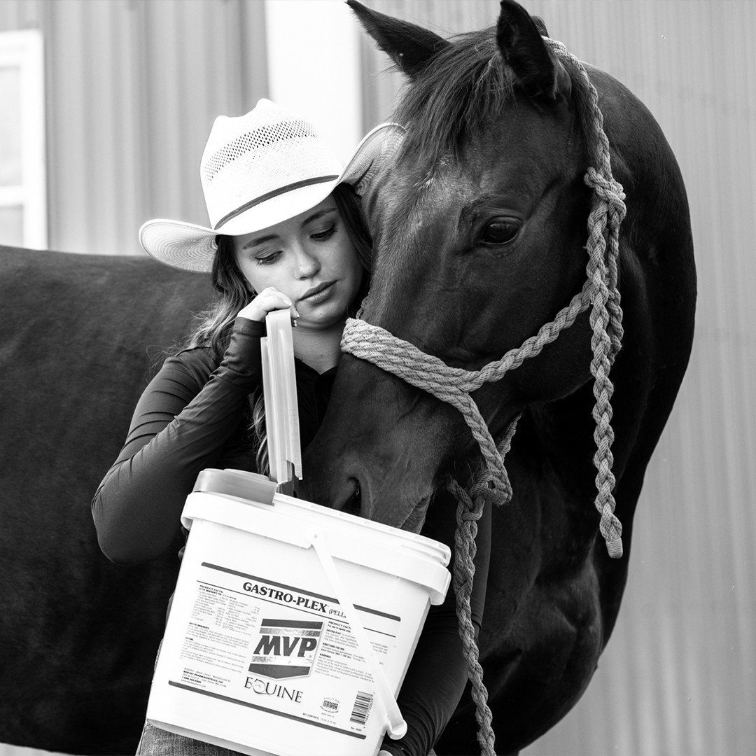 Rider in a cowboy hat resting against her dark horse while holding a GASTRO-PLEX pellet bucket