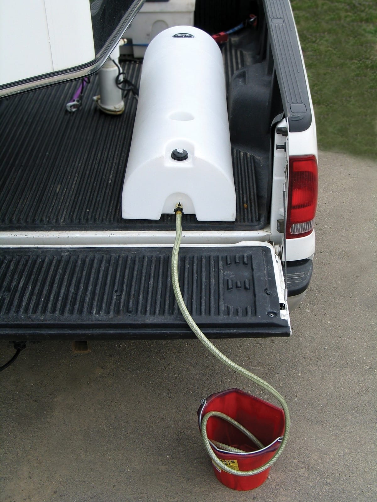 High Country Plastics half-moon lay down water caddy in a pickup bed draining through a hose into a red bucket on the ground