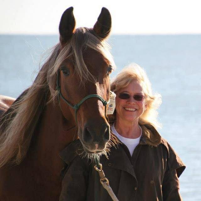 Owner Lindy Griffith standing beside her horse Chief at the ocean shore