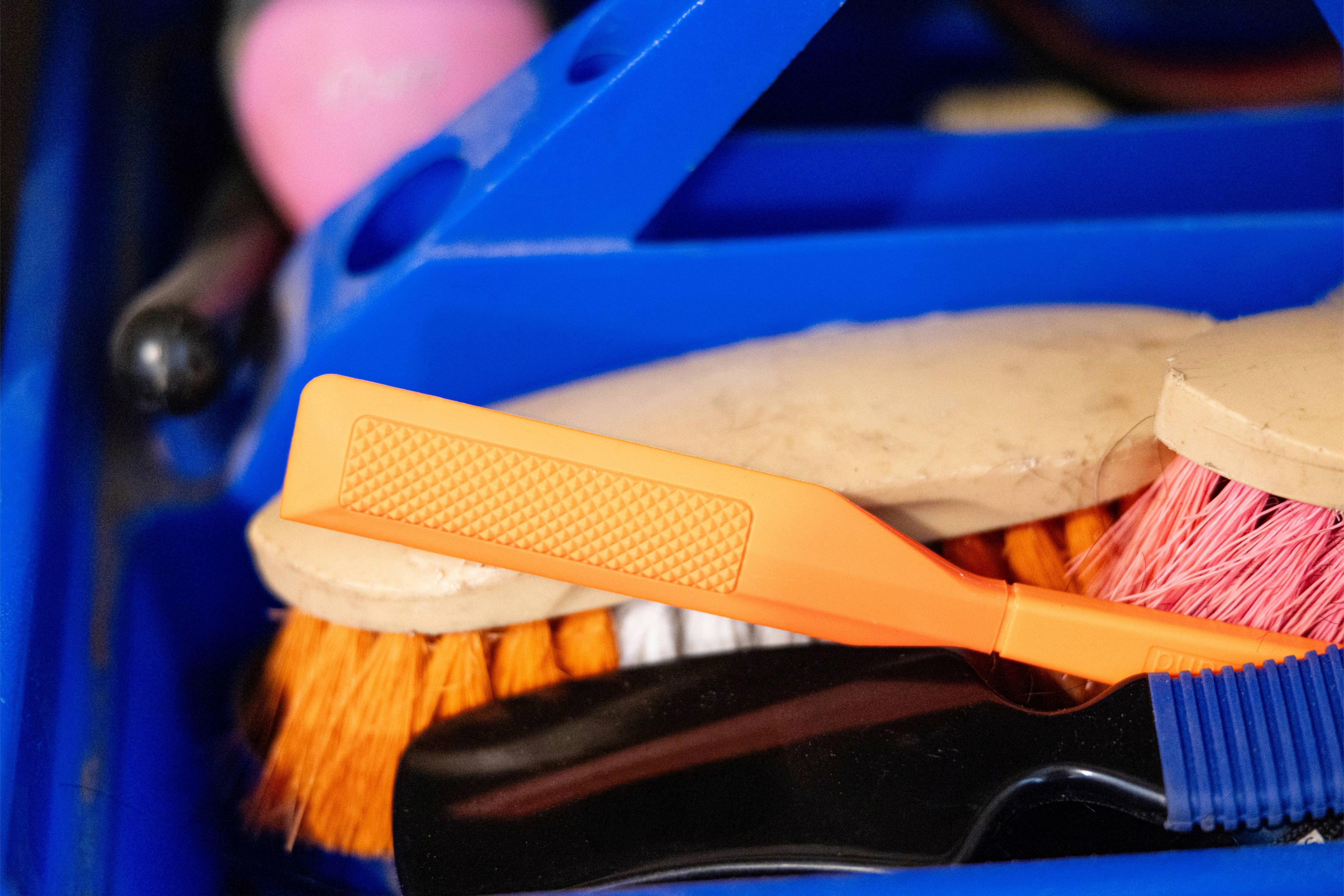 The HoofWand hoof cleaning tool resting in a grooming caddy alongside brushes