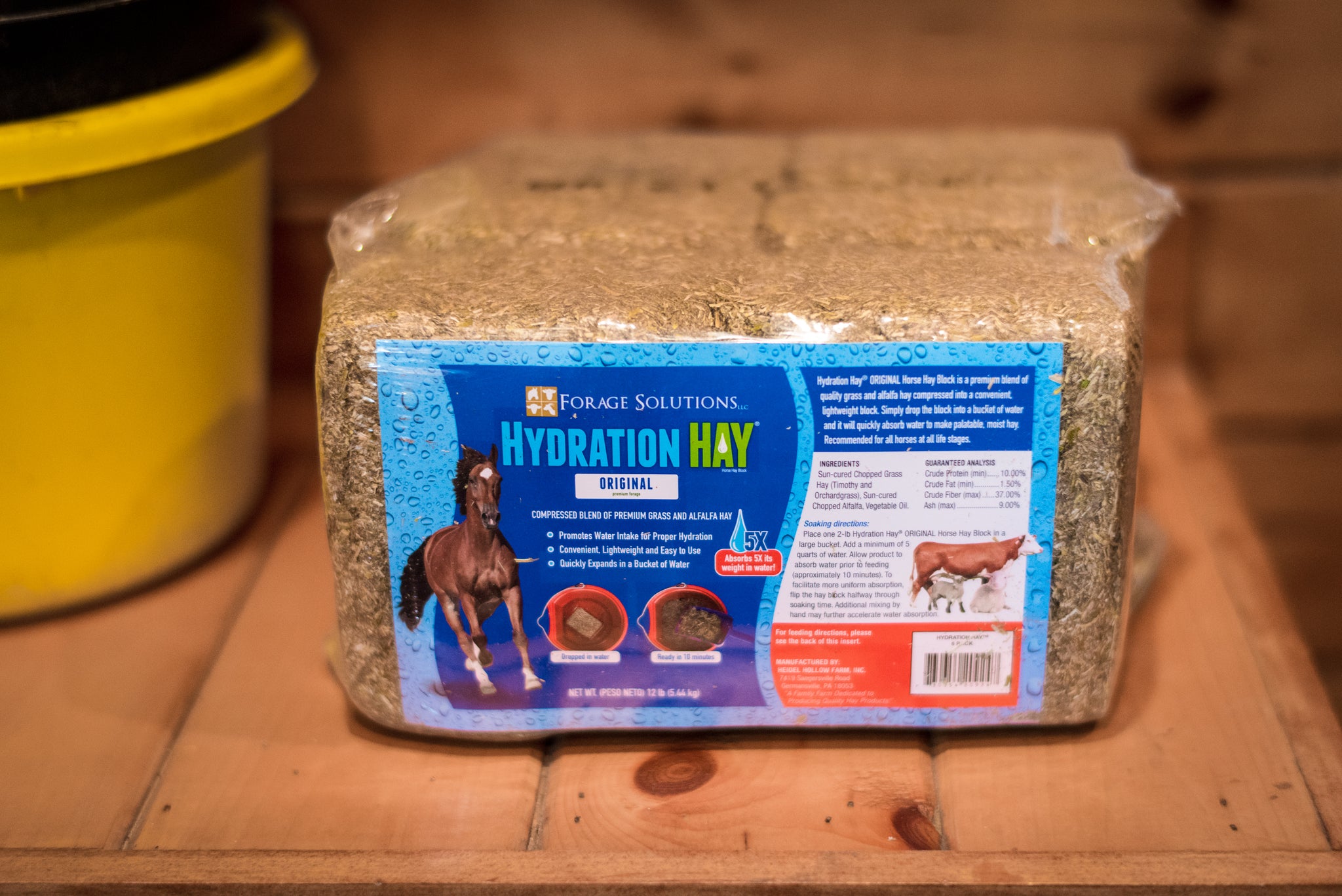 A shrink-wrapped pack of Hydration Hay Original Horse Hay Block resting on a barn workbench