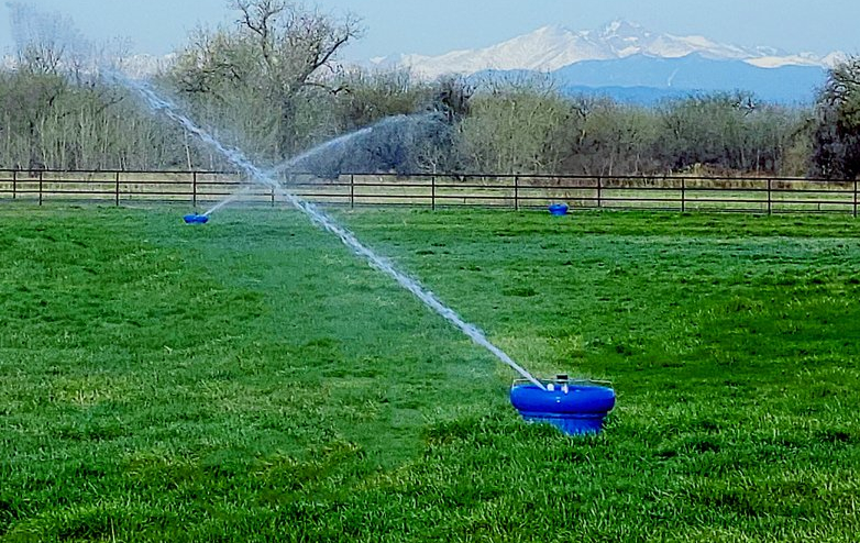 Blue K-Line Irrigation pods spraying water in a fenced grass paddock with snow-capped mountains behind
