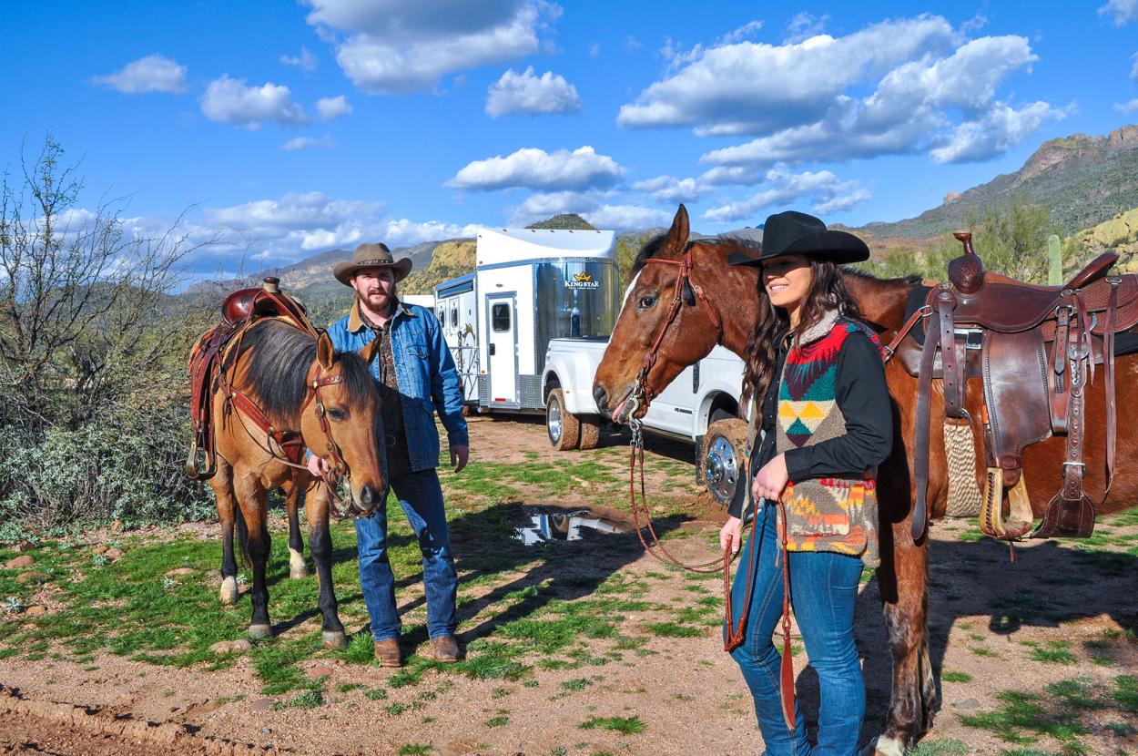 Two riders standing with their saddled horses beside a Kingstar trailer parked in the Arizona high country