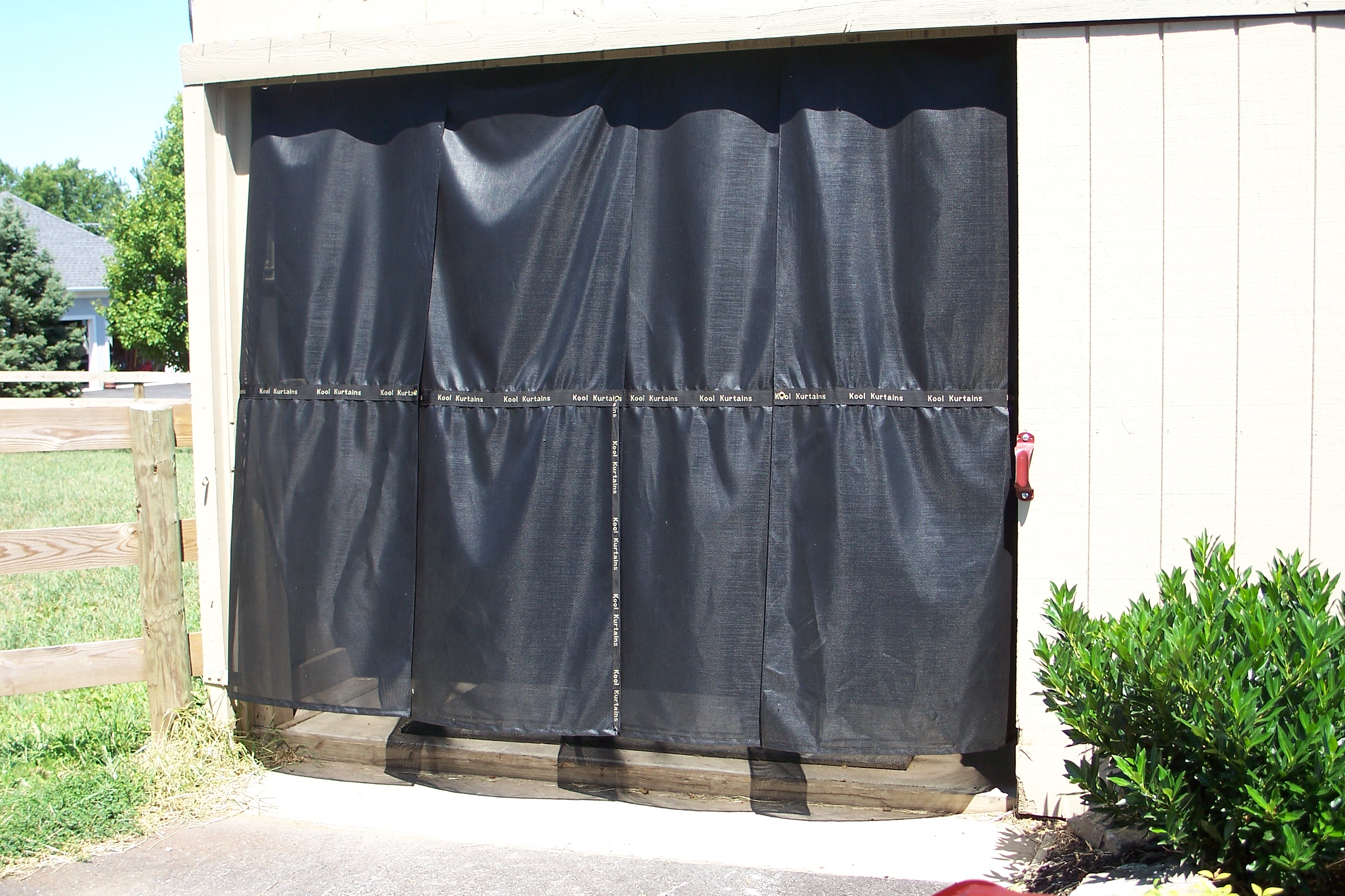 Black CS80 Kool Kurtains panels hanging in a horse barn aisle for shade and bug screening
