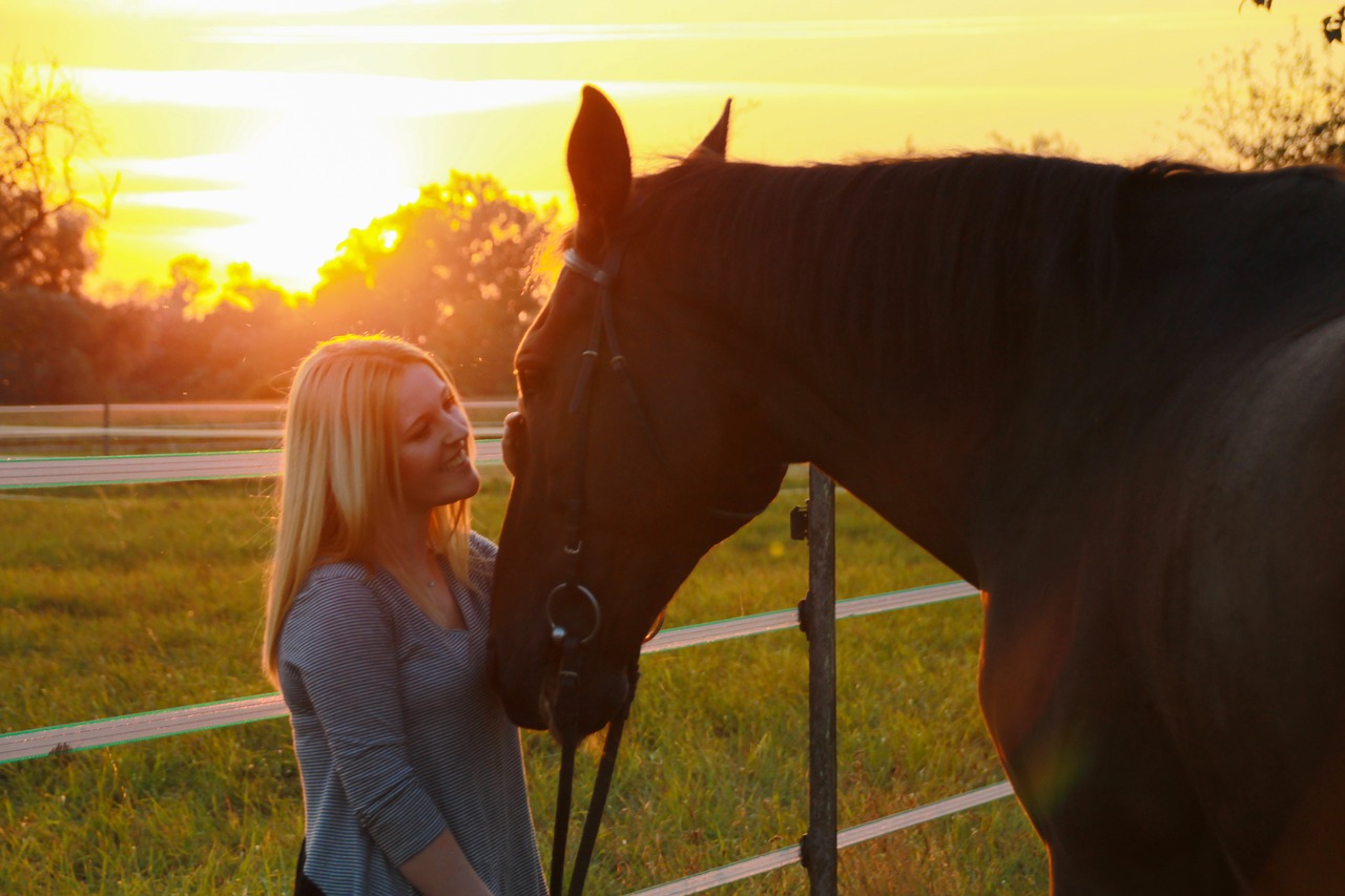 Rider and her horse share a quiet sunset moment in a fenced pasture, conveying long-term equine wellbeing