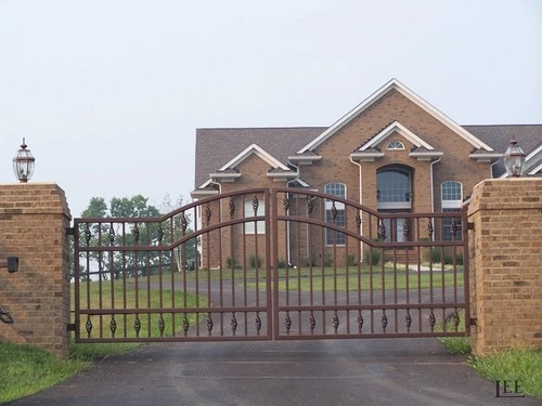 Brown ornamental entrance gates with scrollwork between brick pillars by Lucas Equine Equipment