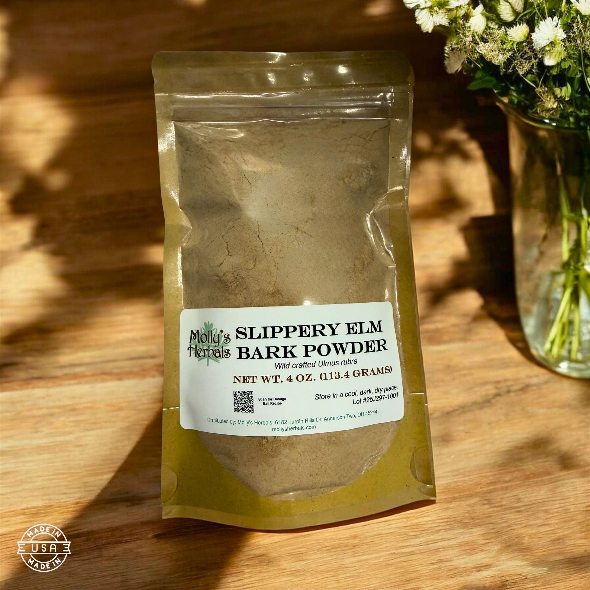 Molly's Herbals slippery elm bark powder pouch on a sunlit wood surface beside fresh flowers