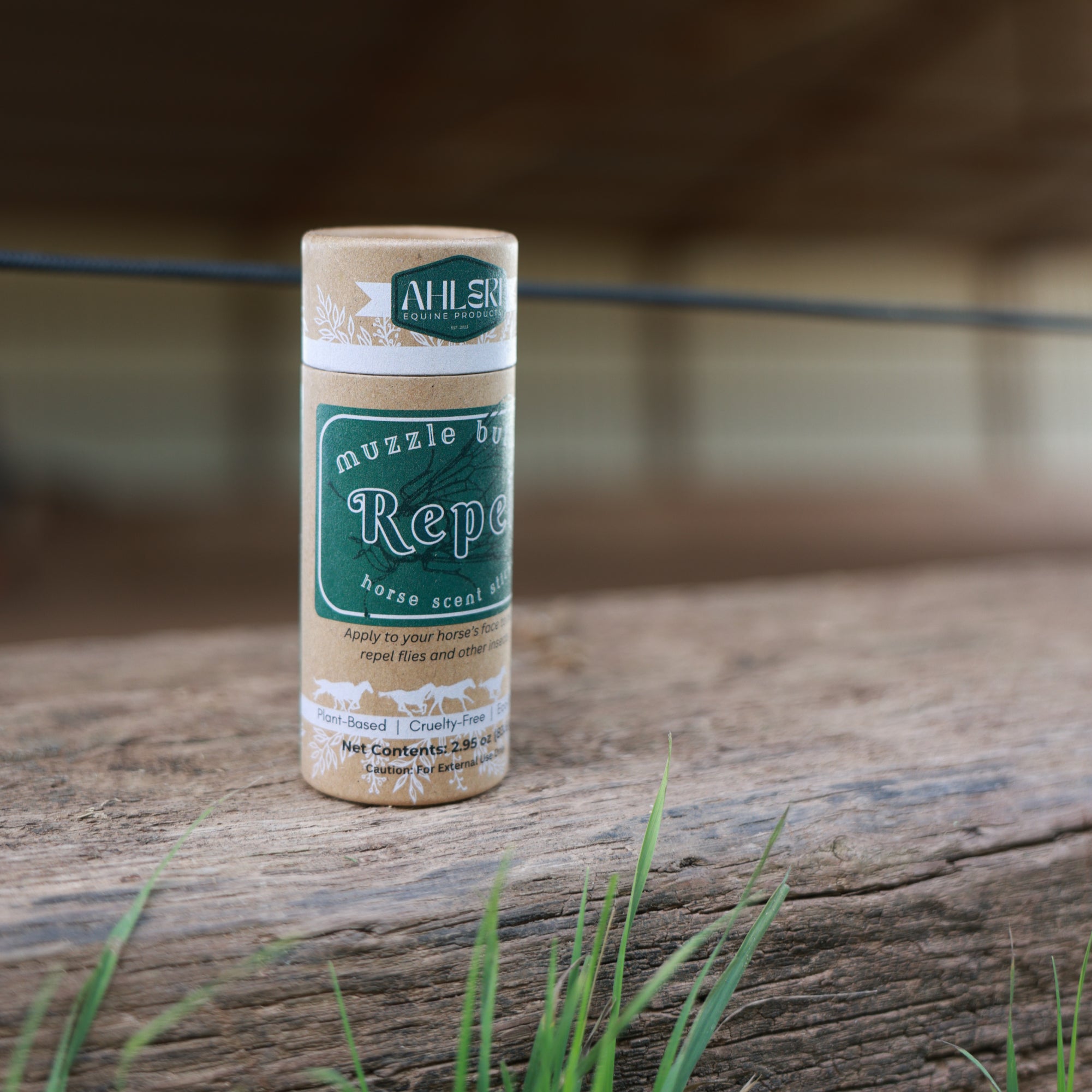 Muzzle Butter Repel balm stick standing on weathered barn wood with green grass nearby