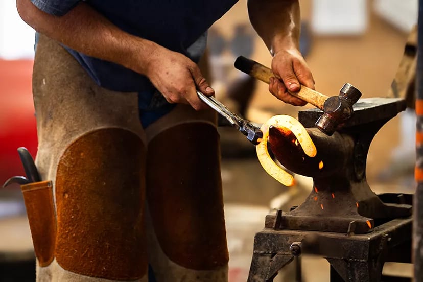 Oklahoma Horseshoeing School student forging a glowing-hot horseshoe on the anvil