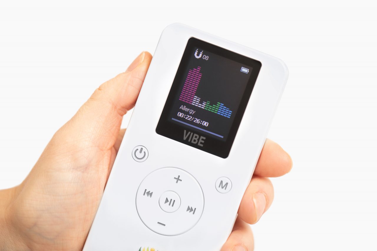 Hand holding the white Resona Health Vibe PEMF device with its color screen showing an active wellness program and timer