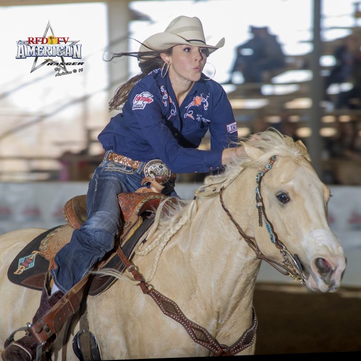 Barrel racer rounding a turn on a palomino quarter horse during a rodeo competition run