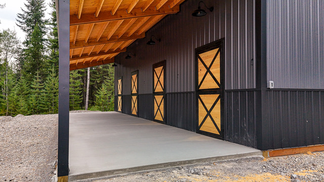 Covered exterior aisle on a black Selkirk barn with four X-brace stall doors in wood and black steel under a timber roof