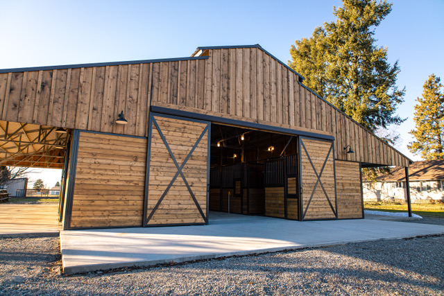 Gable-front Selkirk barn kit in natural wood with black trim, a horse-silhouette door and windows under a blue sky