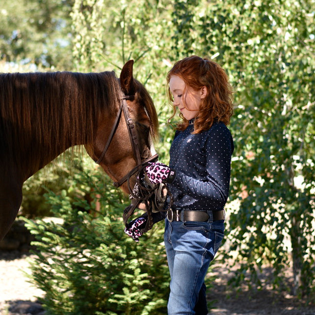 Young rider in pink leopard-print 8600 All Weather gloves standing nose to nose with a bay horse, holding the reins