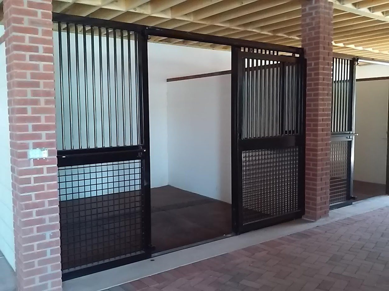 A row of arched grille stall fronts under a timber barn ceiling, built by Sunset Valley Metalcraft