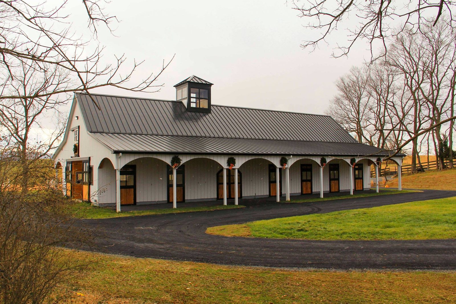 A long brick barn aisle lined with Sunset Valley Metalcraft stall fronts with tack hanging on the wall