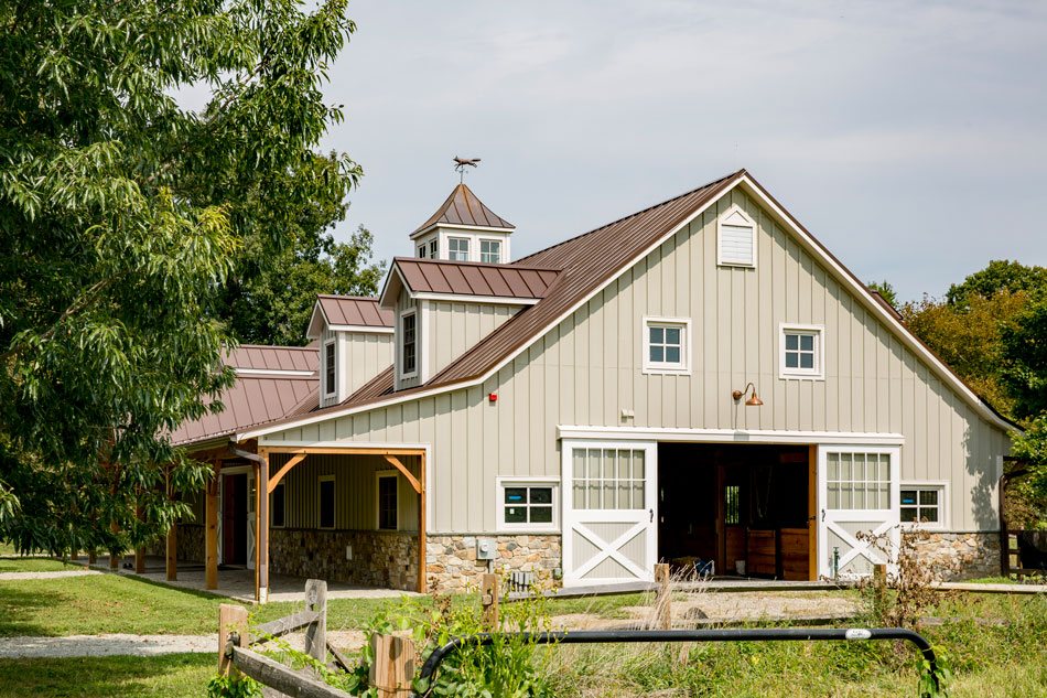 Black European-style horse stall front with an arched top by Sunset Valley Metalcraft, horse looking out over a brick barn aisle