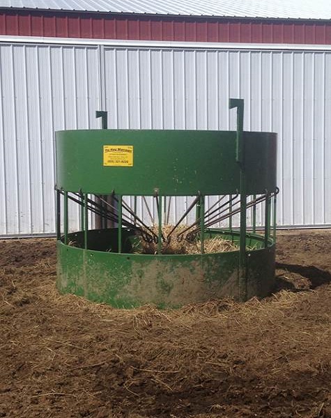 An assembled green Hay Manager round bale feeder set up in a barn lot with loose hay around its base